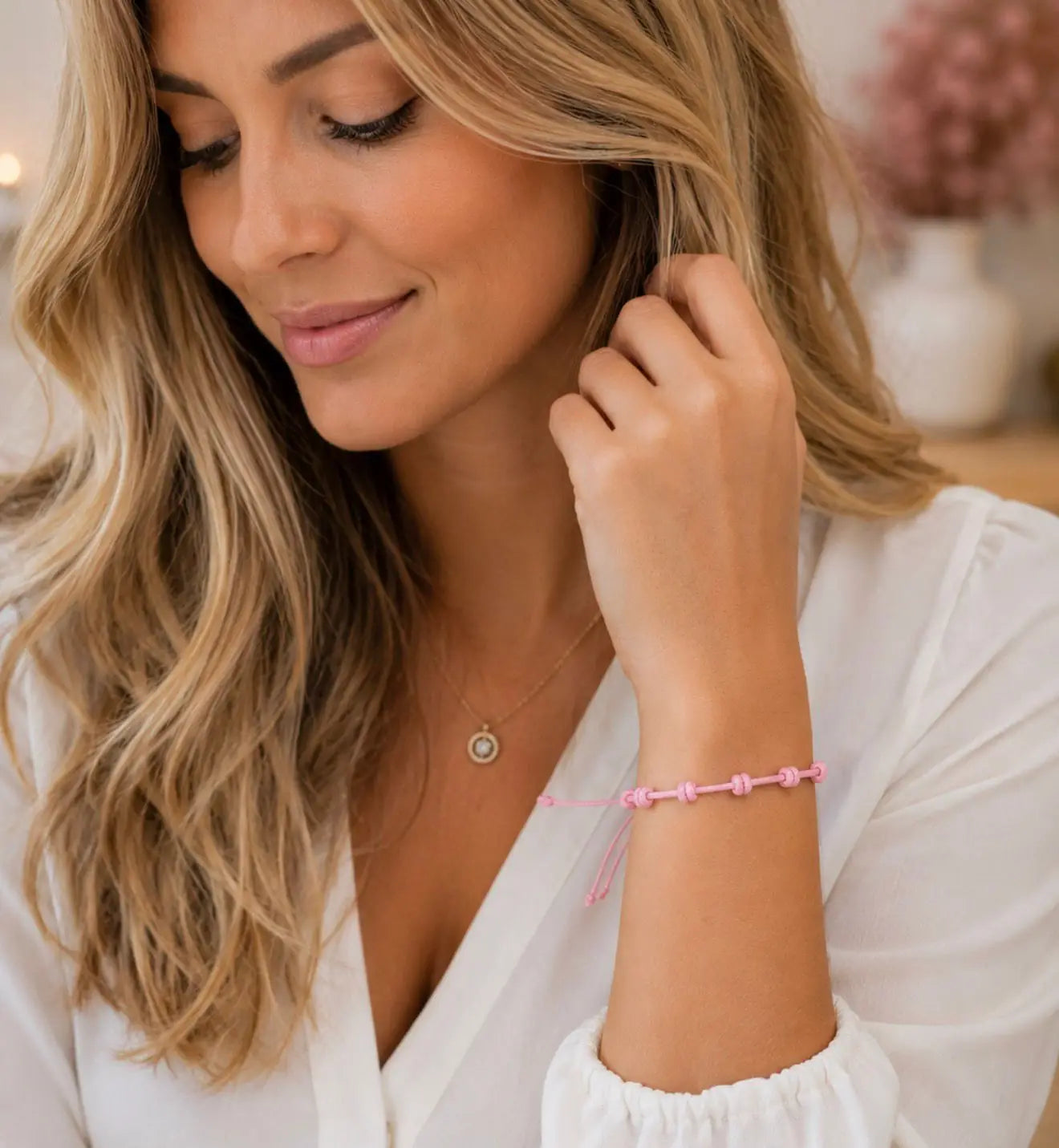 Mulher a usar a pulseira de 7 nós em cordão rosa no pulso, blusa branca
